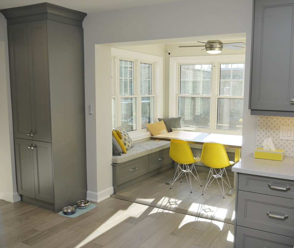 Example of a mid-sized transitional l-shaped light wood floor enclosed kitchen design in Toronto with an undermount sink, recessed-panel cabinets, gray cabinets, quartz countertops, white backsplash, porcelain backsplash, stainless steel appliances and an island