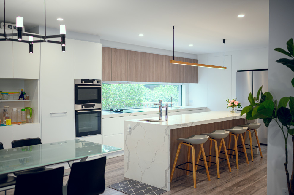 Mid-sized contemporary galley eat-in kitchen in Melbourne with an undermount sink, flat-panel cabinets, white cabinets, quartz benchtops, white splashback, linoleum floors, with island and white benchtop.