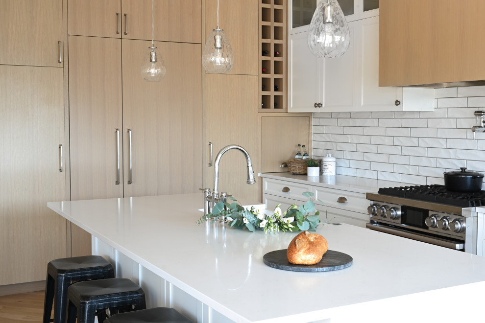 Photo of a transitional l-shaped kitchen in Vancouver with shaker cabinets, quartzite benchtops, white splashback, subway tile splashback, stainless steel appliances, light hardwood floors, with island, white benchtop, an integrated sink, white cabinets and beige floor.