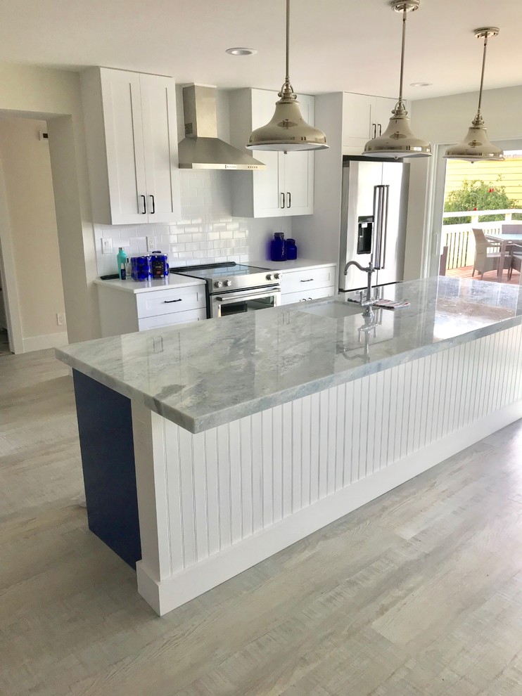 Mid-sized beach style galley eat-in kitchen in Miami with a drop-in sink, shaker cabinets, white cabinets, quartz benchtops, white splashback, ceramic splashback, stainless steel appliances, laminate floors, with island and grey floor.