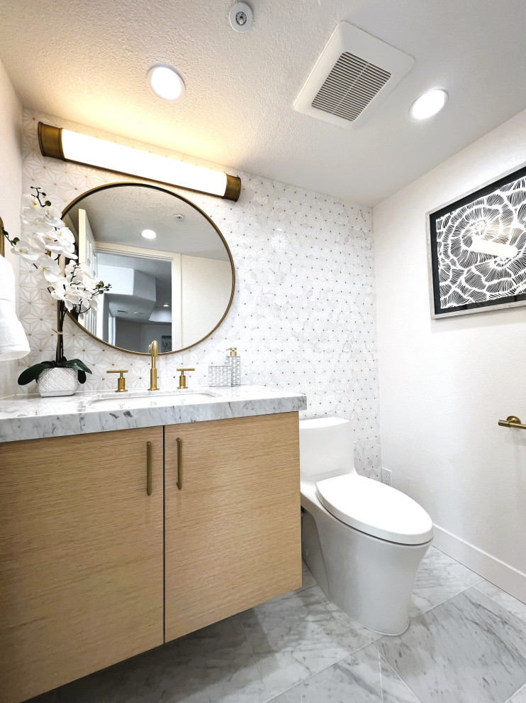 Cette image montre un petit WC et toilettes design en bois clair avec un placard à porte plane, WC à poser, un carrelage blanc, du carrelage en marbre, un mur blanc, un sol en marbre, un lavabo encastré, un plan de toilette en marbre, un sol blanc et meuble-lavabo suspendu.