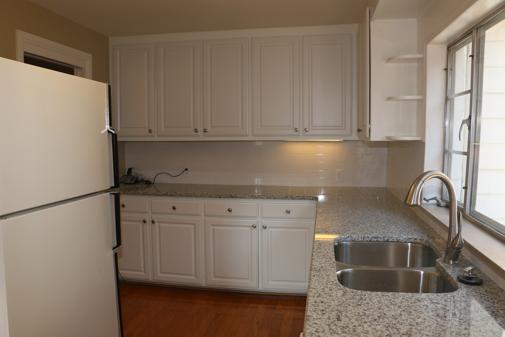 Example of a mid-sized classic l-shaped light wood floor eat-in kitchen design with an undermount sink, raised-panel cabinets, white cabinets, granite countertops, white backsplash, ceramic backsplash and white appliances