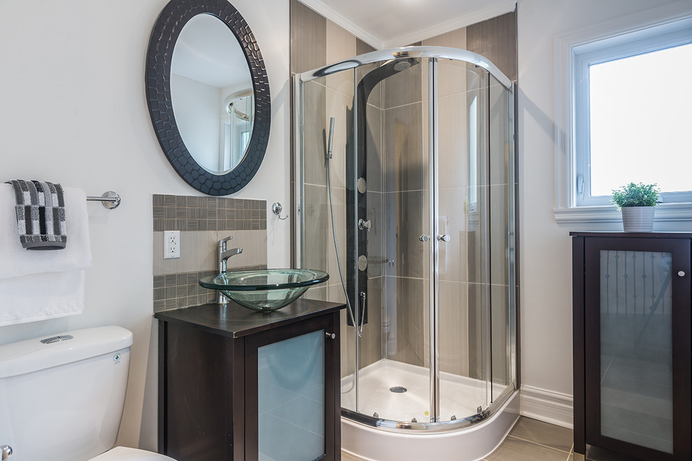 Photo of a small contemporary bathroom in Montreal with a vessel sink, glass-front cabinets, brown cabinets, wood benchtops, a corner shower, a two-piece toilet, multi-coloured tile, porcelain tile, white walls and porcelain floors.