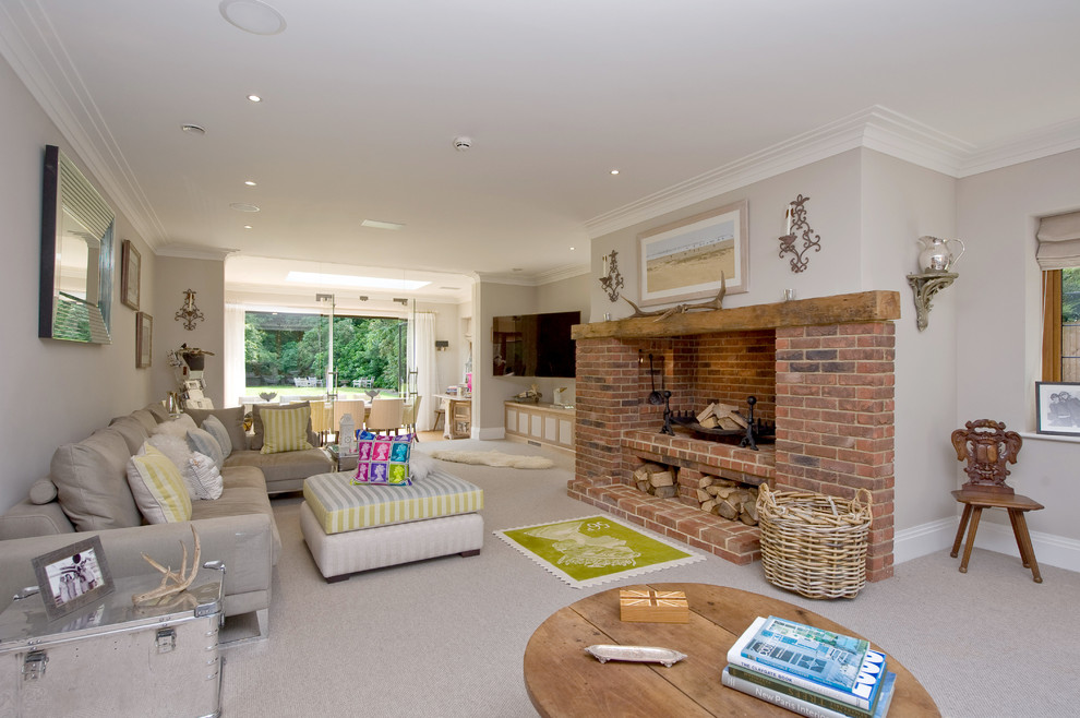 This is an example of a traditional open concept living room in London with grey walls, carpet, a standard fireplace, a brick fireplace surround and a wall-mounted tv.