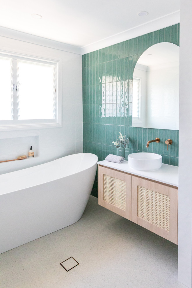 На фото: главная ванная комната среднего размера в морском стиле с светлыми деревянными фасадами, отдельно стоящей ванной, открытым душем, разноцветной плиткой, керамической плиткой, разноцветными стенами, полом из керамогранита, настольной раковиной, столешницей из искусственного камня, белым полом, открытым душем, белой столешницей, нишей, тумбой под одну раковину и подвесной тумбой с