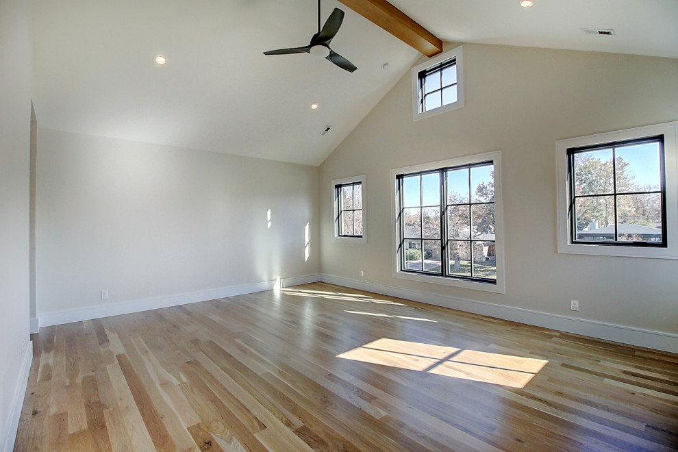 Inspiration for a large transitional master bedroom in Denver with white walls, light hardwood floors, a standard fireplace, a wood fireplace surround, brown floor and exposed beam.
