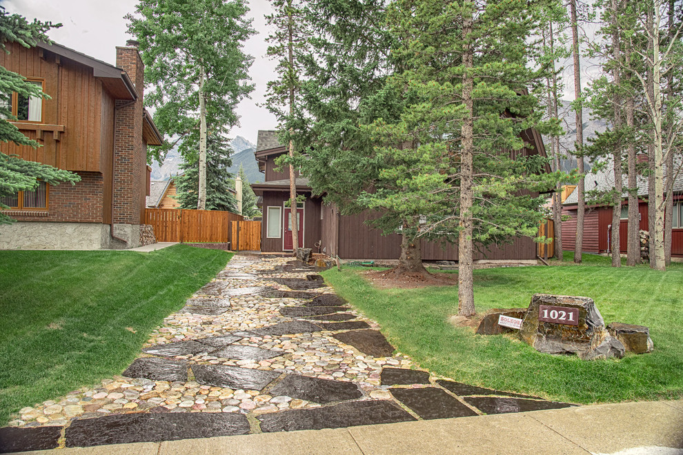 Photo of a mid-sized traditional front yard full sun driveway for spring in Calgary with river rock.