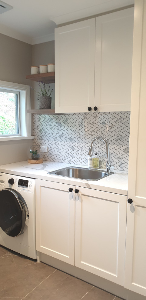 Photo of a mid-sized traditional single-wall dedicated laundry room in Other with a single-bowl sink, shaker cabinets, white cabinets, quartz benchtops, grey walls, porcelain floors, an integrated washer and dryer, grey floor and multi-coloured benchtop.