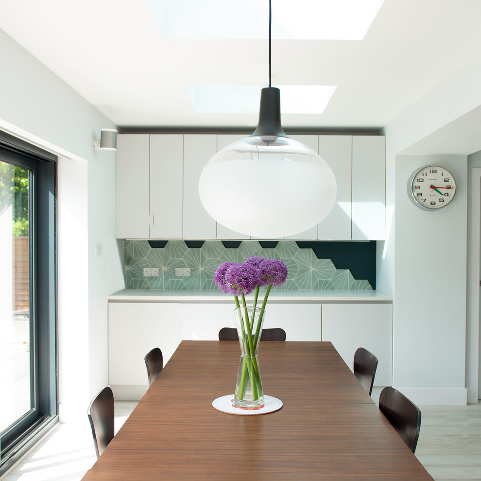 This is an example of a mid-sized contemporary open plan kitchen in Sussex with a drop-in sink, flat-panel cabinets, grey cabinets, quartz benchtops, green splashback, porcelain splashback, panelled appliances, light hardwood floors, with island, white floor and white benchtop.