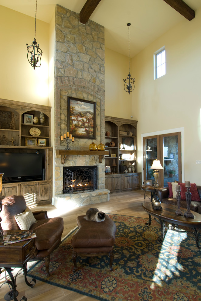 Mediterranean open concept family room in Austin with beige walls, light hardwood floors, a standard fireplace, a stone fireplace surround and a built-in media wall.