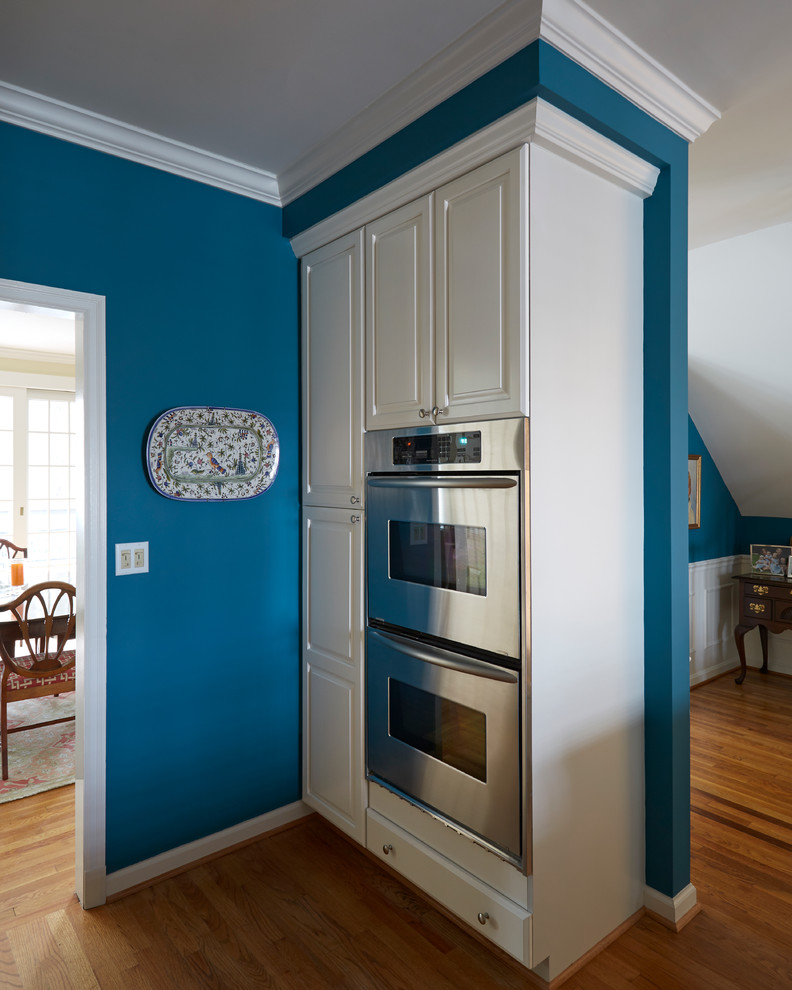 Example of an u-shaped medium tone wood floor open concept kitchen design in Baltimore with white cabinets and stainless steel appliances