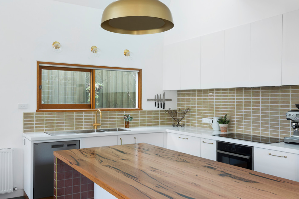 Large modern l-shaped open plan kitchen in Melbourne with a double-bowl sink, white cabinets, wood benchtops, beige splashback, mosaic tile splashback, stainless steel appliances, linoleum floors, with island, green floor and white benchtop.