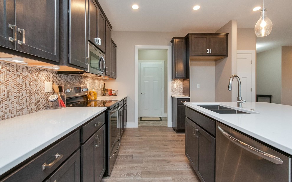 Large transitional single-wall light wood floor and beige floor eat-in kitchen photo in Cedar Rapids with a double-bowl sink, shaker cabinets, dark wood cabinets, solid surface countertops, multicolored backsplash, mosaic tile backsplash and an island