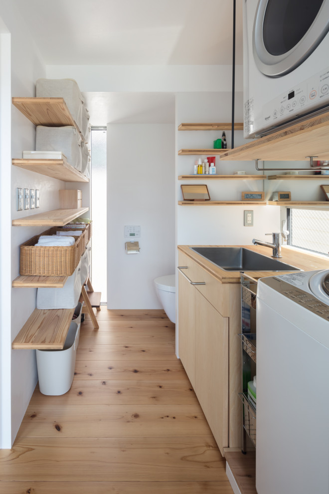 Utility room in Tokyo with white walls, light hardwood flooring and a stacked washer and dryer.