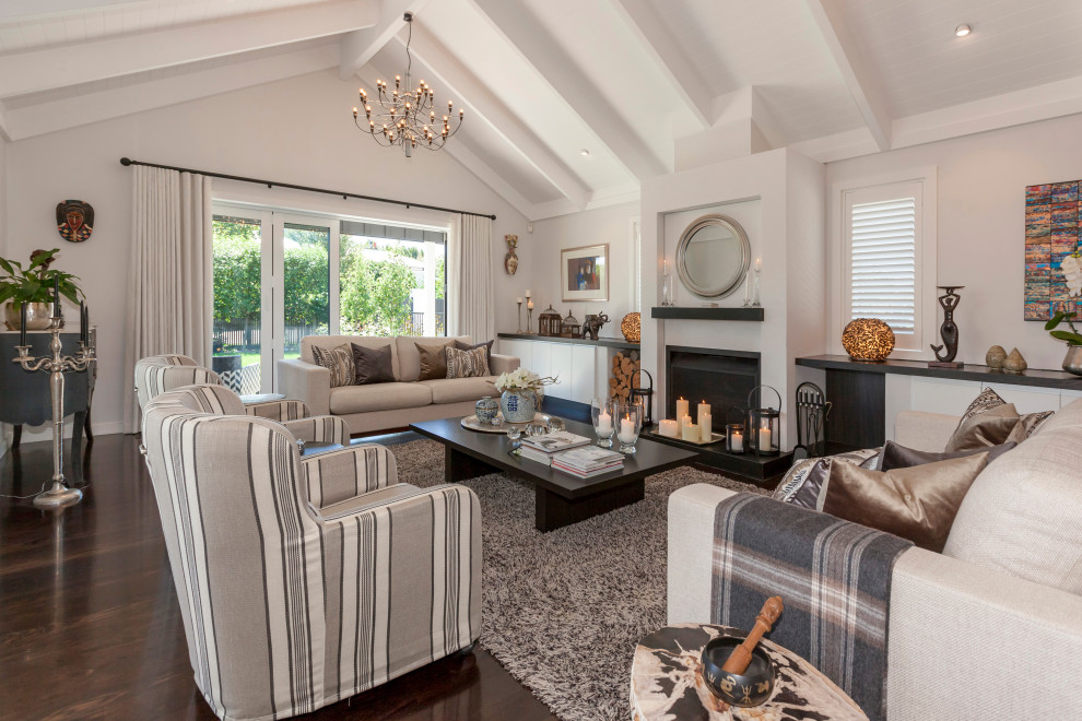 This is an example of an Expansive Open Concept living room in Wellington With White Walls, a Standard Fireplace, a Concrete Fireplace Surround, Brown Floor, Exposed Beam and Dark Hardwood Floors.