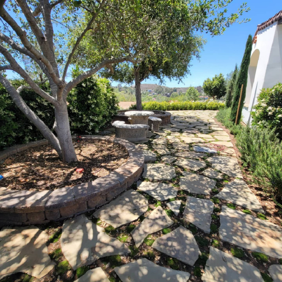 Пример оригинального дизайна: большой летний засухоустойчивый сад на боковом дворе в средиземноморском стиле с полуденной тенью, покрытием из каменной брусчатки и дорожками