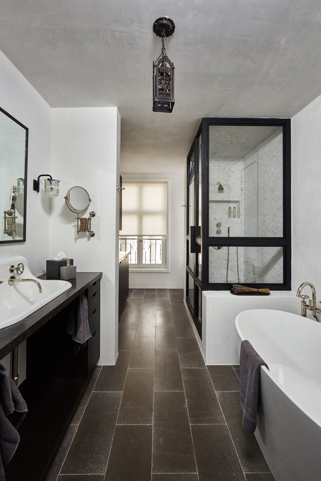 Photo of a mid-sized transitional master wet room bathroom in Los Angeles with flat-panel cabinets, dark wood cabinets, a freestanding tub, a two-piece toilet, white tile, cement tile, white walls, limestone floors, a wall-mount sink, granite benchtops, brown floor and a hinged shower door.