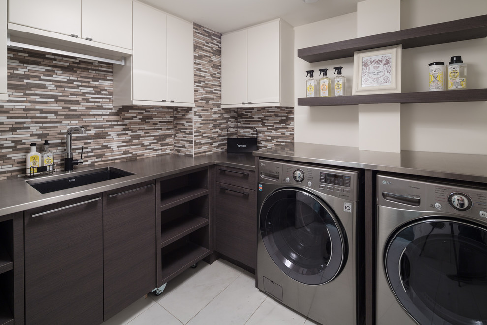 Design ideas for a transitional dedicated laundry room in Ottawa with flat-panel cabinets, white cabinets, stainless steel benchtops, beige walls, porcelain floors, a side-by-side washer and dryer and an undermount sink.