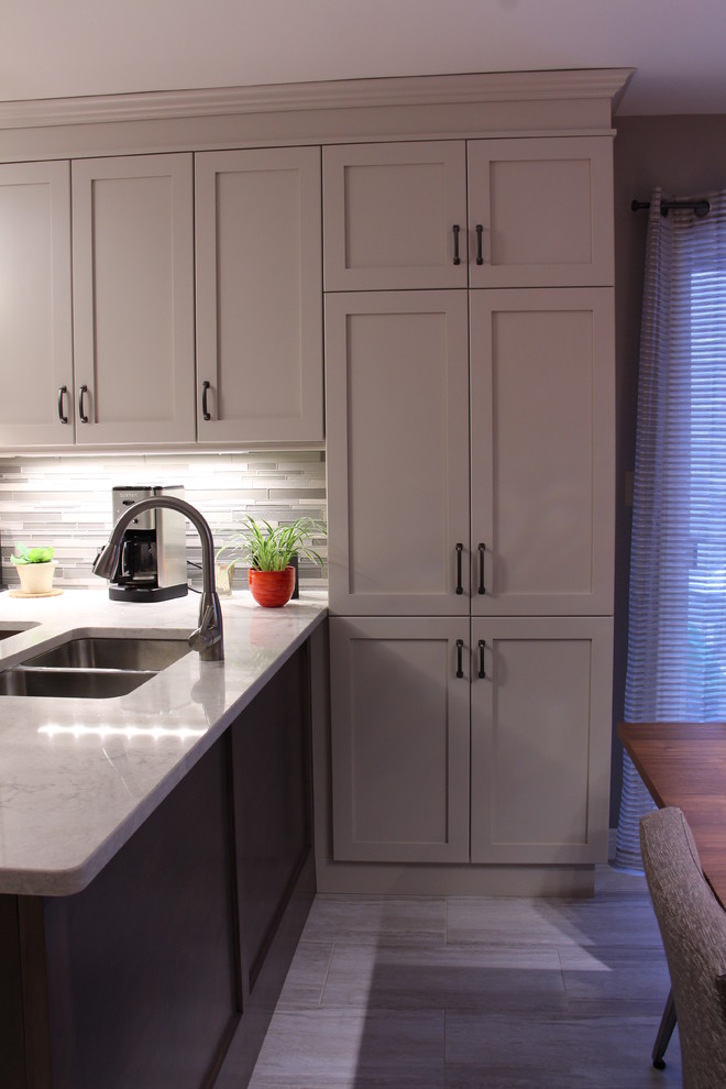 Mid-sized transitional u-shaped ceramic tile and beige floor eat-in kitchen photo in Toronto with a double-bowl sink, shaker cabinets, gray cabinets, solid surface countertops, gray backsplash, glass sheet backsplash, stainless steel appliances and no island