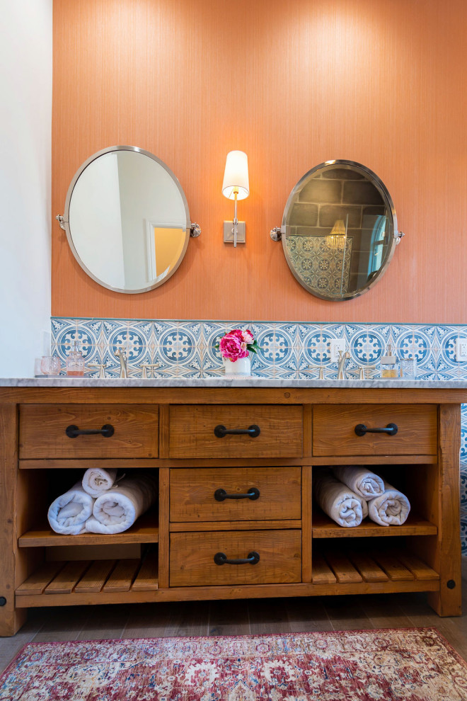 This is an example of a mid-sized country master bathroom in Los Angeles with furniture-like cabinets, distressed cabinets, a freestanding tub, a corner shower, a one-piece toilet, gray tile, ceramic tile, orange walls, ceramic floors, a drop-in sink, marble benchtops, brown floor, a hinged shower door, white benchtops, a shower seat, a double vanity, a freestanding vanity and wallpaper.