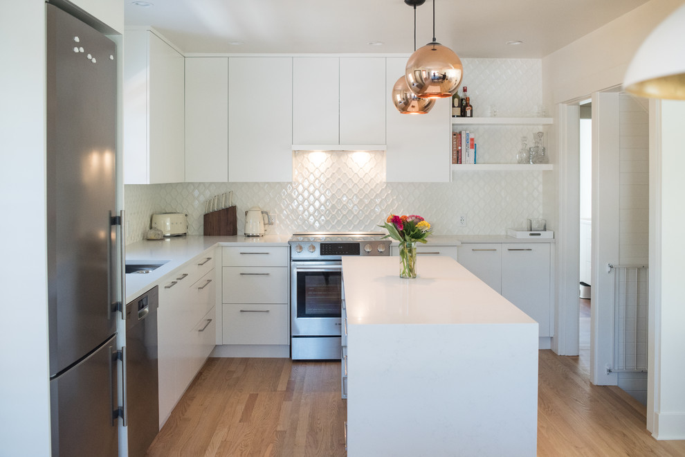 Inspiration for a mid-sized transitional l-shaped light wood floor eat-in kitchen remodel in Vancouver with an undermount sink, flat-panel cabinets, white cabinets, quartz countertops, white backsplash, ceramic backsplash, stainless steel appliances and an island