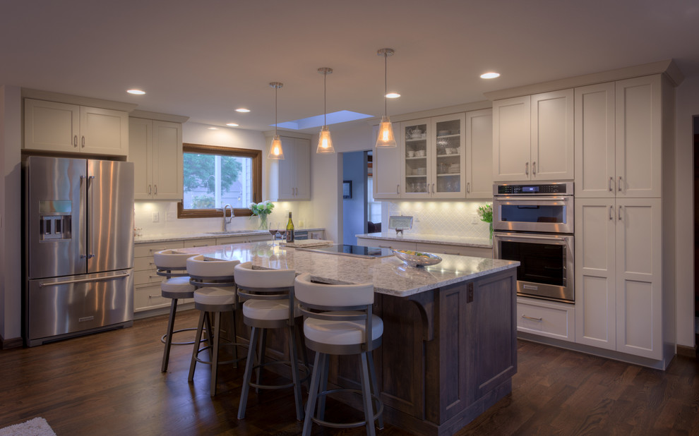 Inspiration for a large transitional dark wood floor kitchen remodel in Denver with an undermount sink, shaker cabinets, solid surface countertops, white backsplash, ceramic backsplash, stainless steel appliances and an island