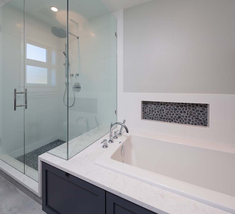 Mid-sized modern bathroom with shaker cabinets, grey cabinets, a drop-in tub, a corner shower, a one-piece toilet, white tile, white walls, an undermount sink, grey floor, a hinged shower door and white benchtops.