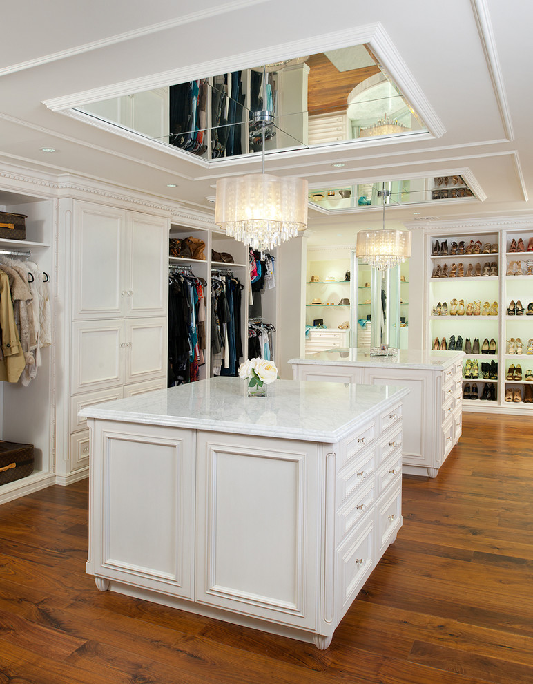 Photo of an expansive traditional women's dressing room in Other with beaded inset cabinets, white cabinets, brown floor and dark hardwood floors.