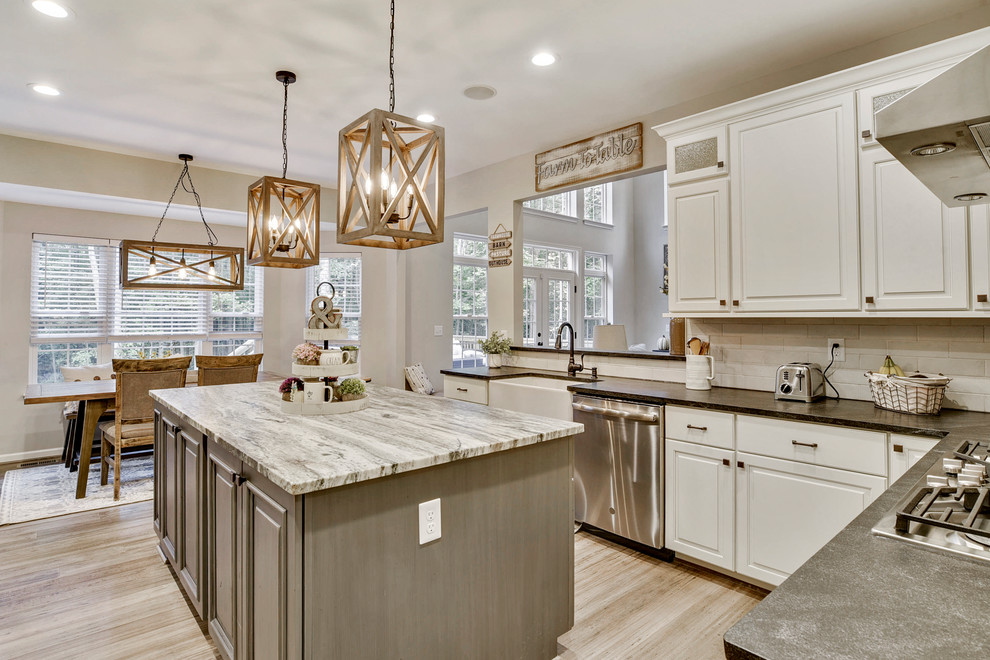 Photo of a mid-sized country u-shaped eat-in kitchen in DC Metro with a farmhouse sink, raised-panel cabinets, beige cabinets, granite benchtops, white splashback, ceramic splashback, stainless steel appliances, bamboo floors, with island, grey floor and grey benchtop.