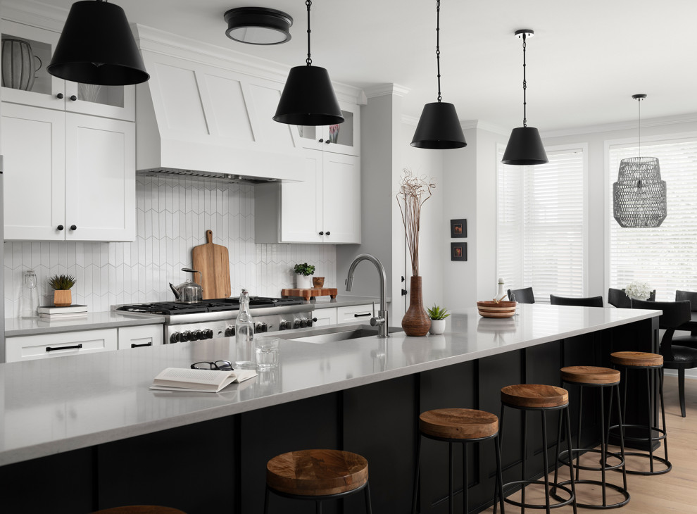 Inspiration for a mid-sized transitional galley light wood floor open concept kitchen remodel in Chicago with an undermount sink, shaker cabinets, white cabinets, quartz countertops, white backsplash, ceramic backsplash, stainless steel appliances, an island and gray countertops
