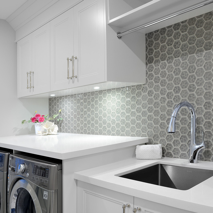 Large transitional single-wall utility room in Toronto with an undermount sink, recessed-panel cabinets, white cabinets, quartz benchtops, grey splashback, glass tile splashback, grey walls, porcelain floors, a side-by-side washer and dryer and white benchtop.