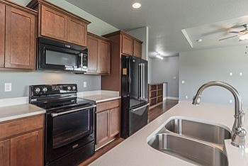 Example of a mid-sized transitional l-shaped medium tone wood floor eat-in kitchen design with an undermount sink, recessed-panel cabinets, medium tone wood cabinets, quartz countertops, black appliances and an island