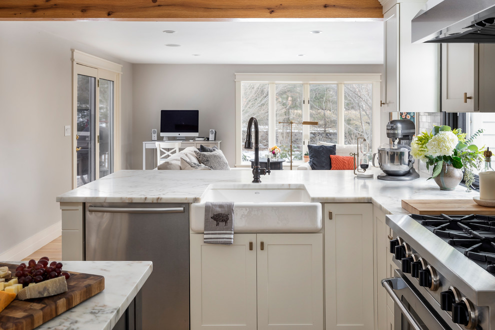 Inspiration for a large transitional l-shaped light wood floor and brown floor kitchen remodel in Boston with a farmhouse sink, yellow cabinets, marble countertops, white backsplash, marble backsplash, stainless steel appliances, an island and white countertops