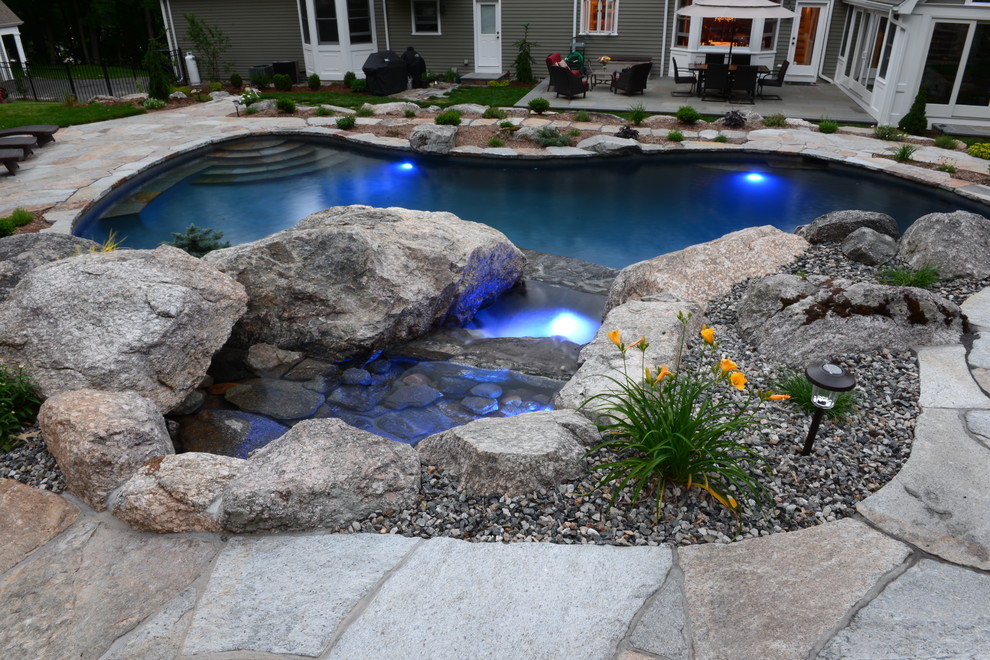 This is an example of a mid-sized tropical backyard custom-shaped natural pool in New York with a hot tub and natural stone pavers.