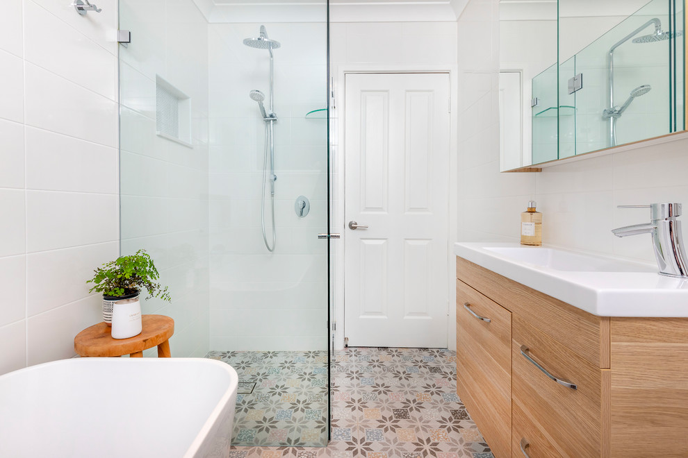 This is an example of a mid-sized contemporary master bathroom in Sydney with raised-panel cabinets, light wood cabinets, a freestanding tub, a corner shower, a two-piece toilet, white tile, ceramic tile, white walls, porcelain floors, a vessel sink, engineered quartz benchtops, multi-coloured floor, a hinged shower door and multi-coloured benchtops.