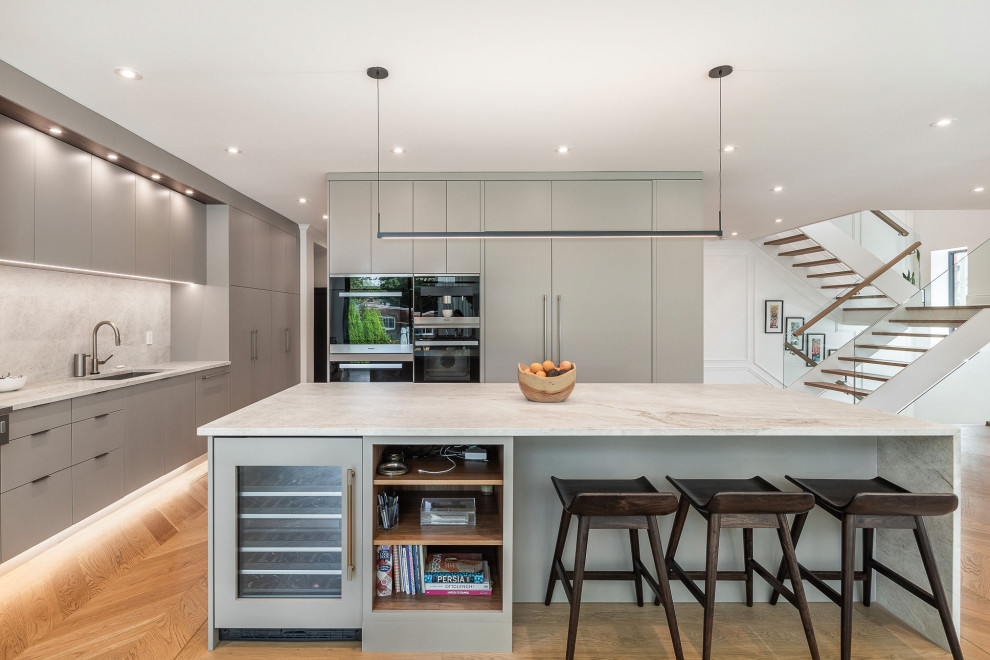 Example of a large eclectic l-shaped light wood floor and beige floor open concept kitchen design with an undermount sink, flat-panel cabinets, green cabinets, quartzite countertops, beige backsplash, quartz backsplash, paneled appliances, an island and beige countertops