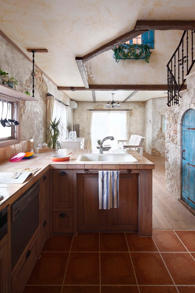 Mediterranean l-shaped eat-in kitchen in Other with a drop-in sink, recessed-panel cabinets, tile benchtops, terra-cotta floors, a peninsula and brown floor.