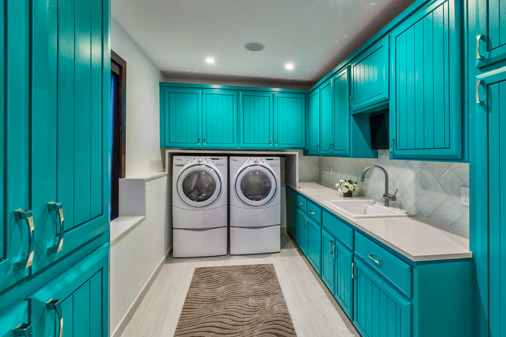 Photo of a large eclectic u-shaped utility room in Denver with raised-panel cabinets, blue cabinets, solid surface benchtops, white walls, a side-by-side washer and dryer, laminate floors, grey floor and a drop-in sink.
