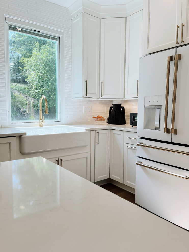Inspiration for a large transitional l-shaped light wood floor and beige floor eat-in kitchen remodel with a farmhouse sink, shaker cabinets, white cabinets, quartz countertops, white backsplash, ceramic backsplash, white appliances, an island and white countertops