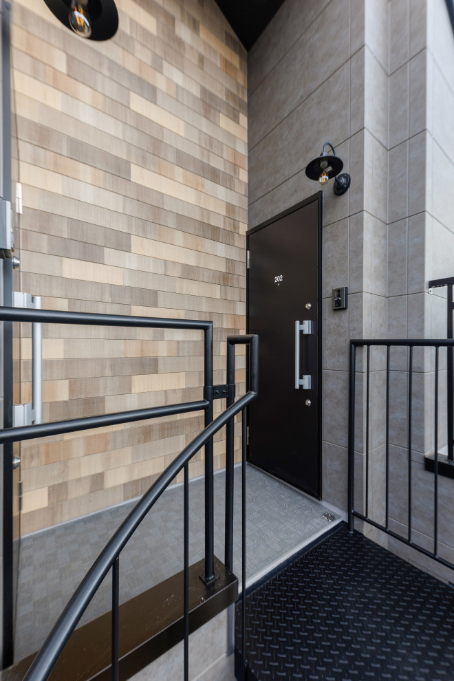 Foto på en liten funkis ingång och ytterdörr, med grå väggar, plywoodgolv, en svart dörr och brunt golv