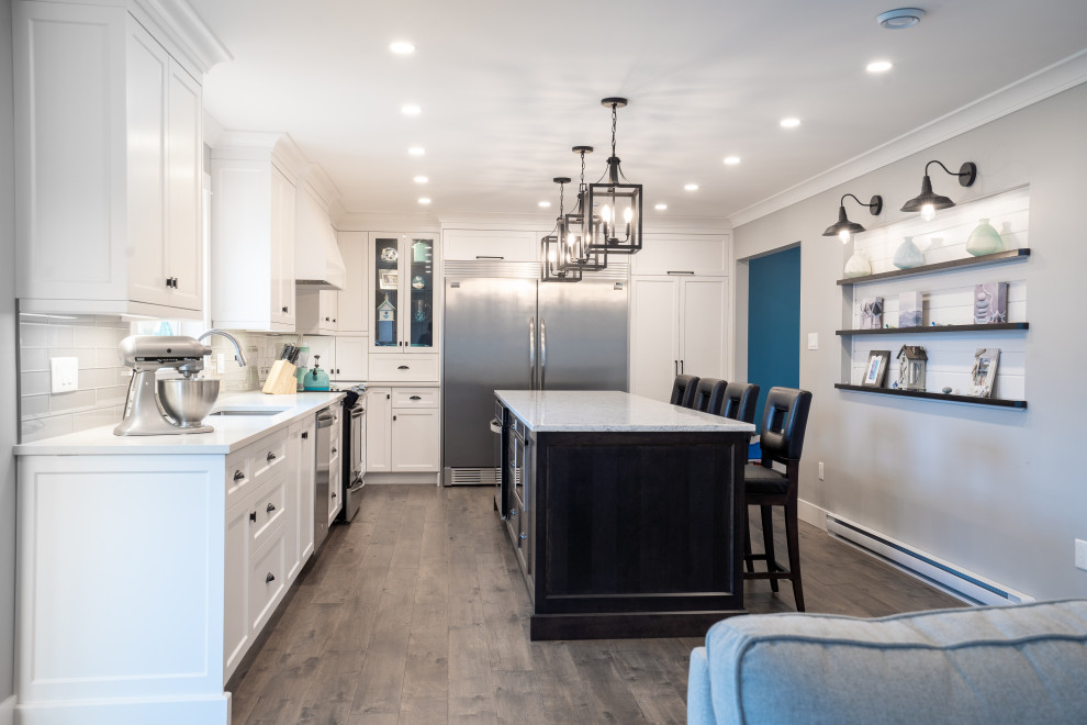 Inspiration for a large transitional l-shaped medium tone wood floor and brown floor kitchen remodel with an undermount sink, white cabinets, quartz countertops, white backsplash, glass tile backsplash, stainless steel appliances, an island and white countertops