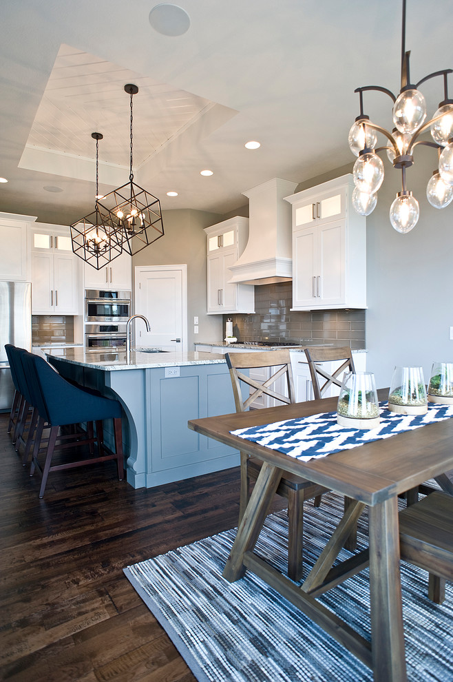 Mid-sized transitional l-shaped dark wood floor and brown floor eat-in kitchen photo with a farmhouse sink, raised-panel cabinets, white cabinets, quartz countertops, gray backsplash, glass tile backsplash, stainless steel appliances and an island