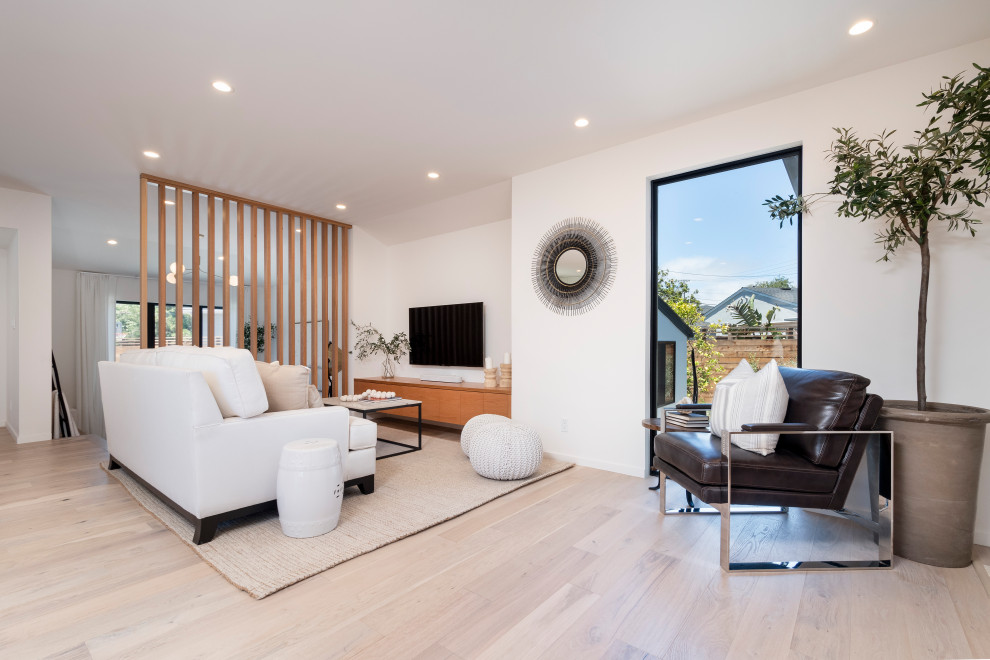 Modelo de salón abierto y blanco minimalista de tamaño medio con paredes blancas, suelo de madera clara y televisor colgado en la pared