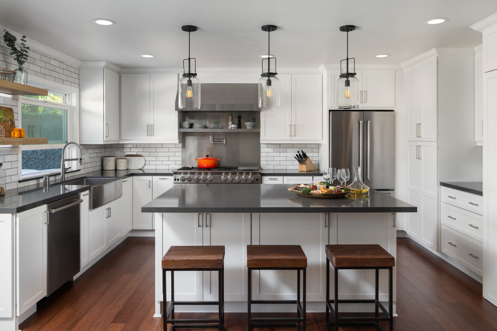 Klassisk inredning av ett mellanstort grå grått kök, med en rustik diskho, luckor med infälld panel, vita skåp, bänkskiva i kvarts, vitt stänkskydd, stänkskydd i keramik, rostfria vitvaror, mellanmörkt trägolv, en köksö och brunt golv