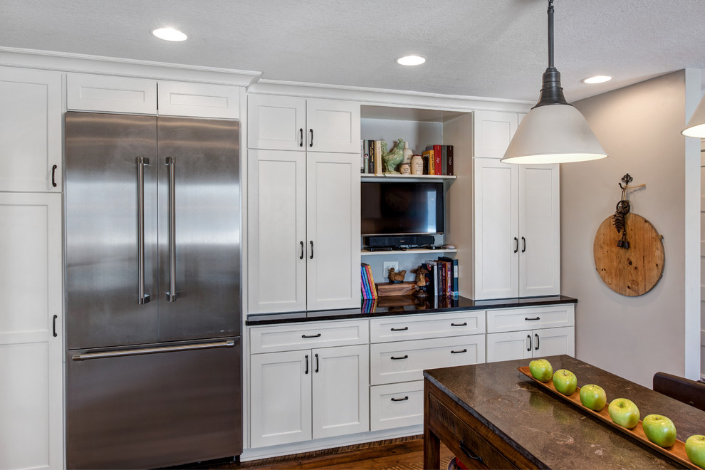 Photo of a country l-shaped kitchen in Minneapolis with a farmhouse sink, shaker cabinets, white cabinets, white splashback, subway tile splashback, stainless steel appliances, dark hardwood floors and with island.
