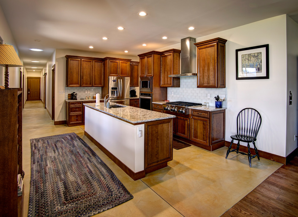 Mid-sized transitional l-shaped concrete floor kitchen photo with an undermount sink, raised-panel cabinets, dark wood cabinets, granite countertops, white backsplash, glass tile backsplash, stainless steel appliances and an island