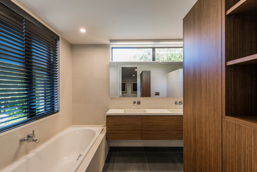 Contemporary bathroom in Christchurch with flat-panel cabinets, dark wood cabinets, a drop-in tub, beige walls and an integrated sink.