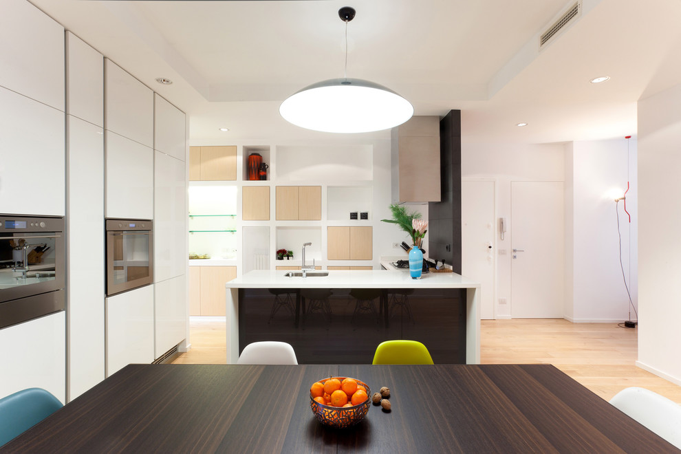 Design ideas for a contemporary l-shaped open plan kitchen in Milan with an undermount sink, flat-panel cabinets, white cabinets, solid surface benchtops and light hardwood floors.