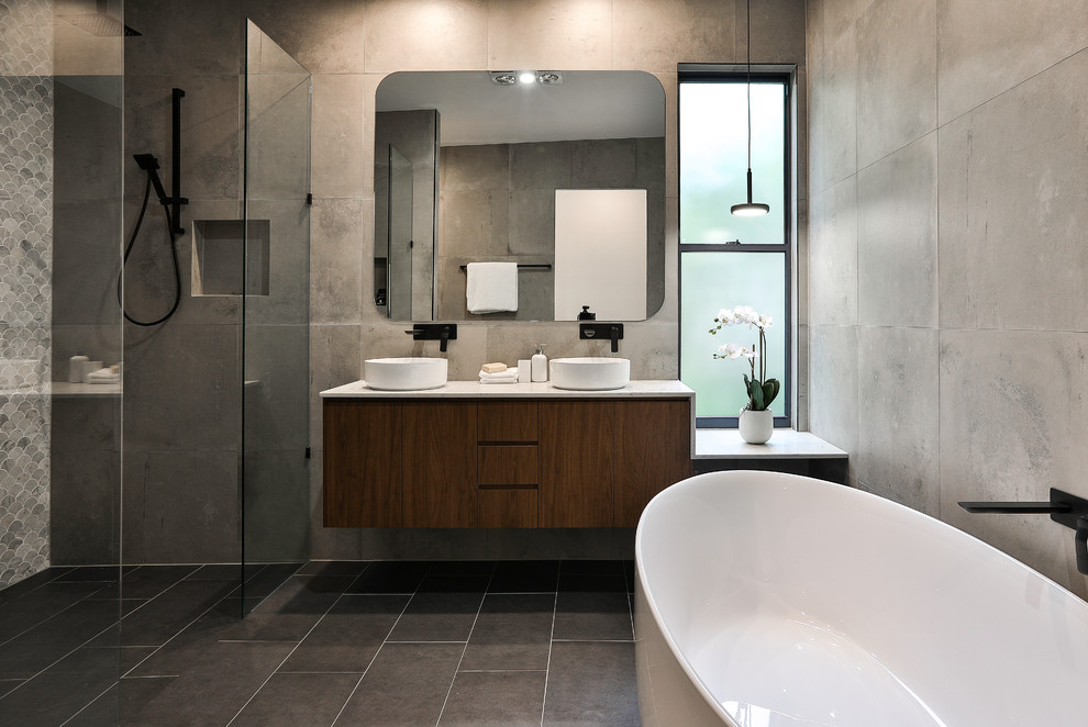 Photo of a contemporary master bathroom in Brisbane with flat-panel cabinets, medium wood cabinets, a freestanding tub, an alcove shower, gray tile, grey walls, a vessel sink, grey floor, an open shower and grey benchtops.