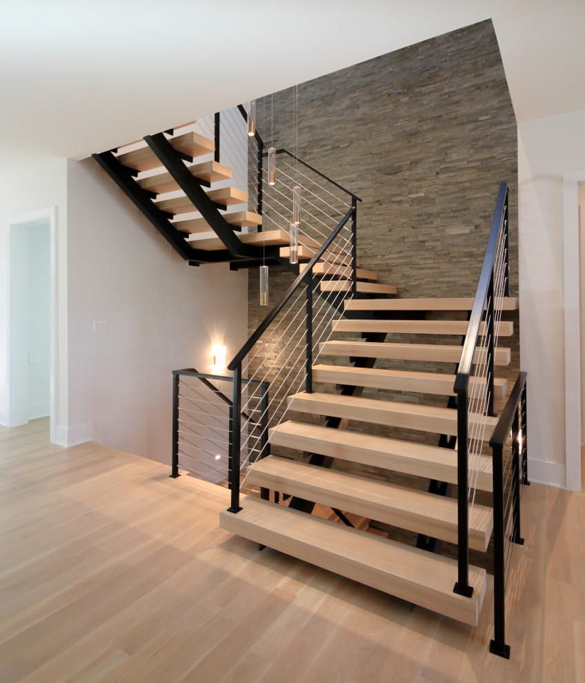 Idée de décoration pour un grand escalier flottant bohème avec des marches en bois, un garde-corps en métal et un mur en parement de brique.